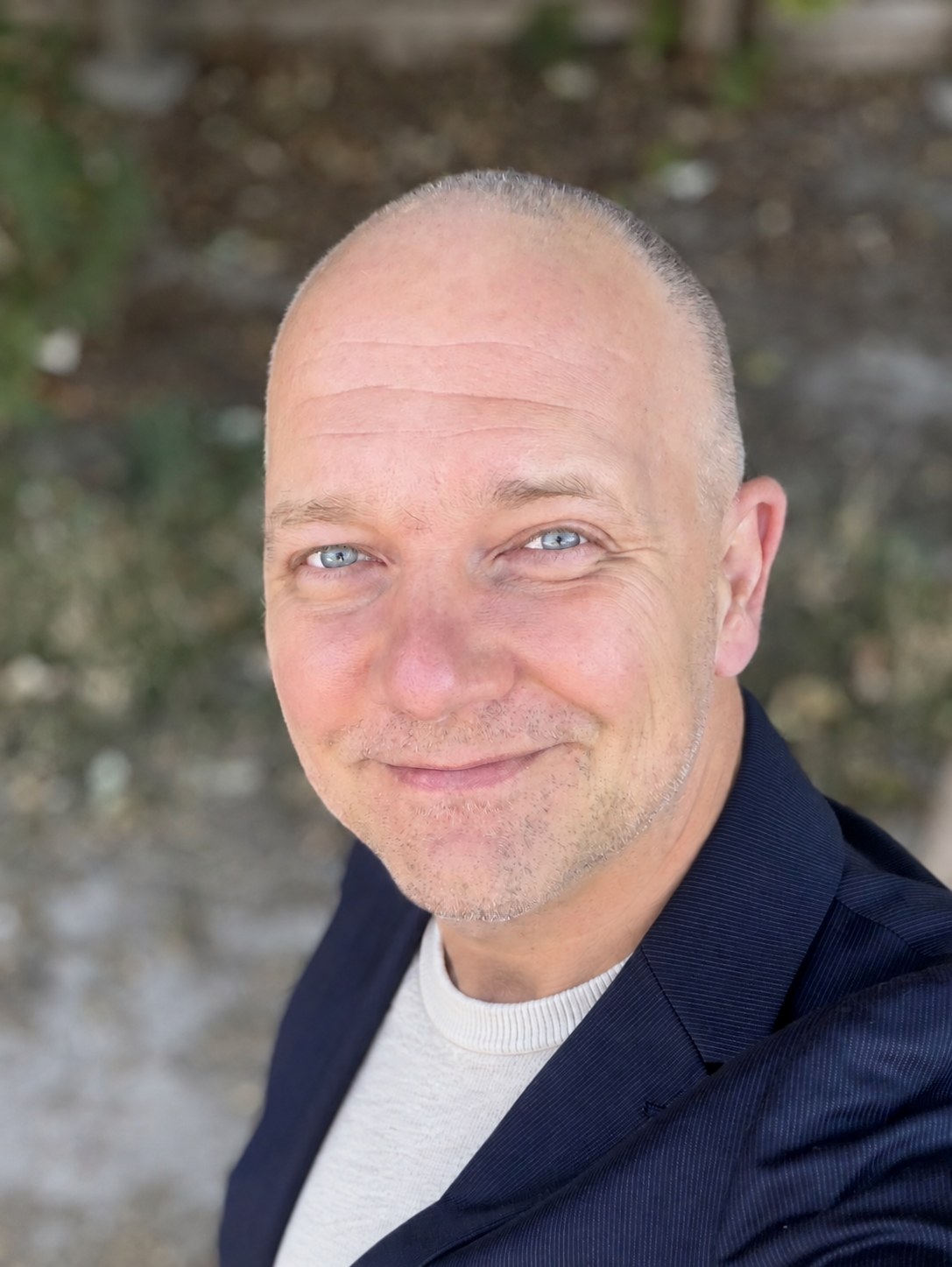 Portrait of Milan Steskal in a navy blazer and cream sweater, smiling