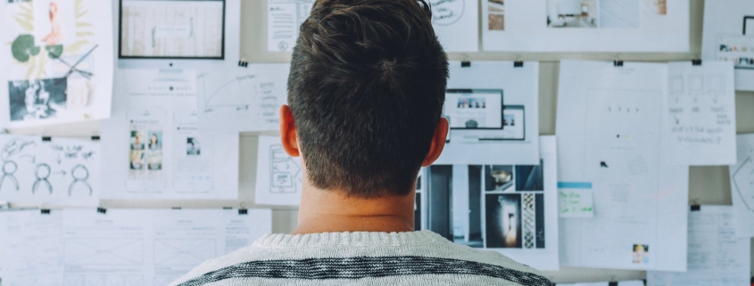 man wearing black and white stripe shirt looking at white printer papers on the wall